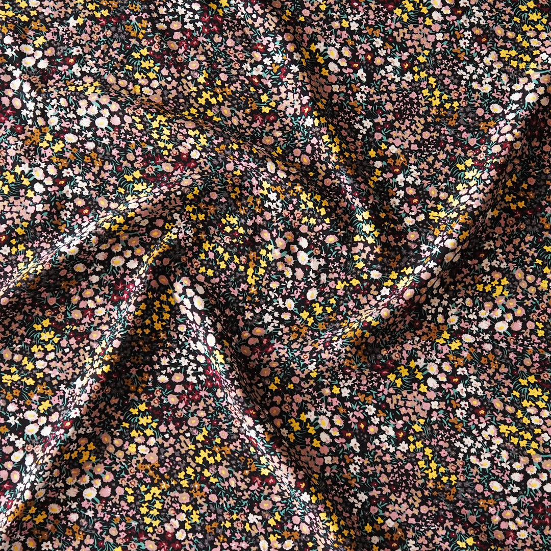 A close-up of draped fabric with an all-over dense floral and dot pattern in pink, yellow, white, and dark green on a dark background.
