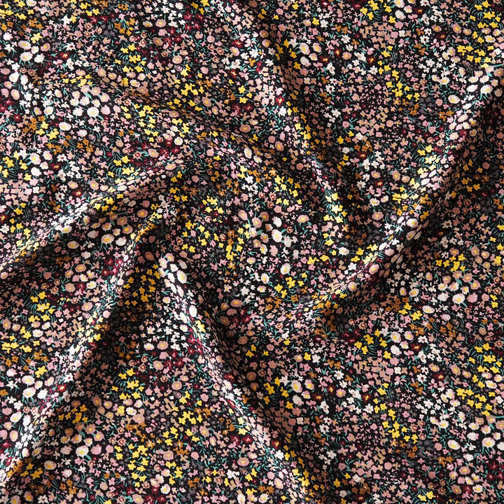 A close-up of draped fabric with an all-over dense floral and dot pattern in pink, yellow, white, and dark green on a dark background.