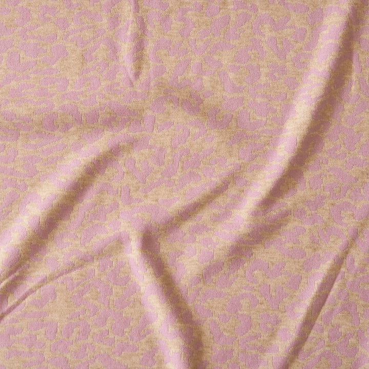 A close-up of a pink and beige patterned fabric with a textured jacquard or damask design, shown with soft folds.