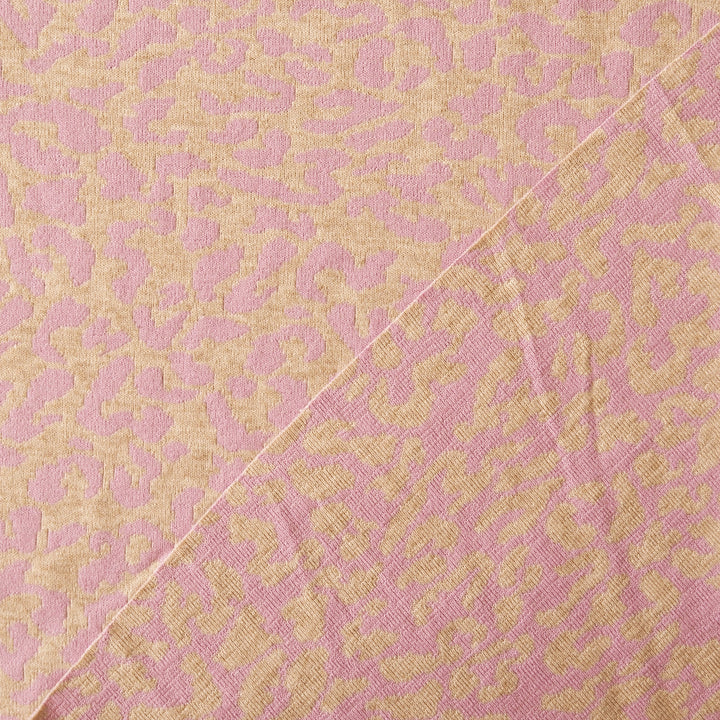 A close-up of a woven fabric with an abstract floral jacquard pattern in dusty pink and warm beige, featuring a diagonal seam.
