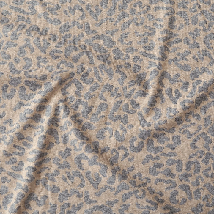 A close-up of a textured fabric with a beige base and a muted blue-gray leopard or dalmatian-style spot pattern, shown with soft folds.