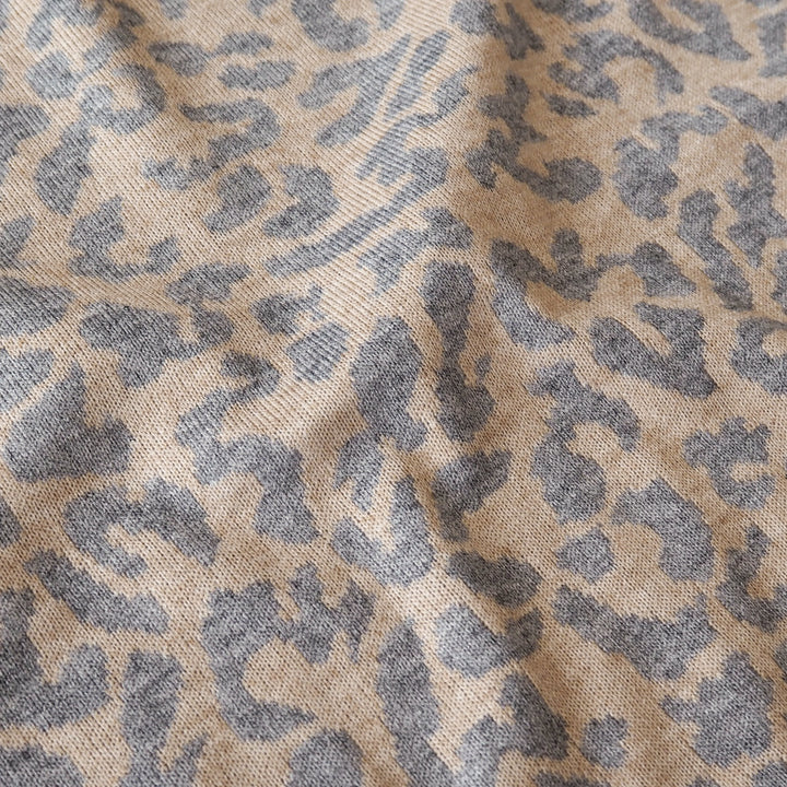 A close-up of a woven fabric with an abstract leopard-like pattern in dark gray on a warm beige background.
