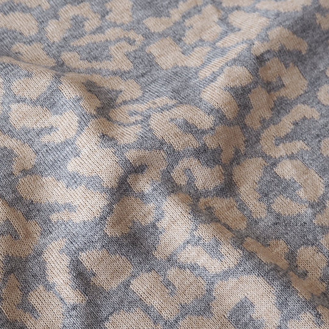 A close-up of a woven textile with an abstract leopard-like pattern in beige and muted blue-gray.