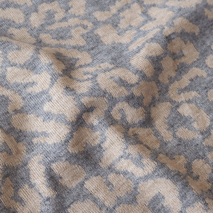 A close-up of a woven textile with an abstract leopard-like pattern in beige and muted blue-gray.