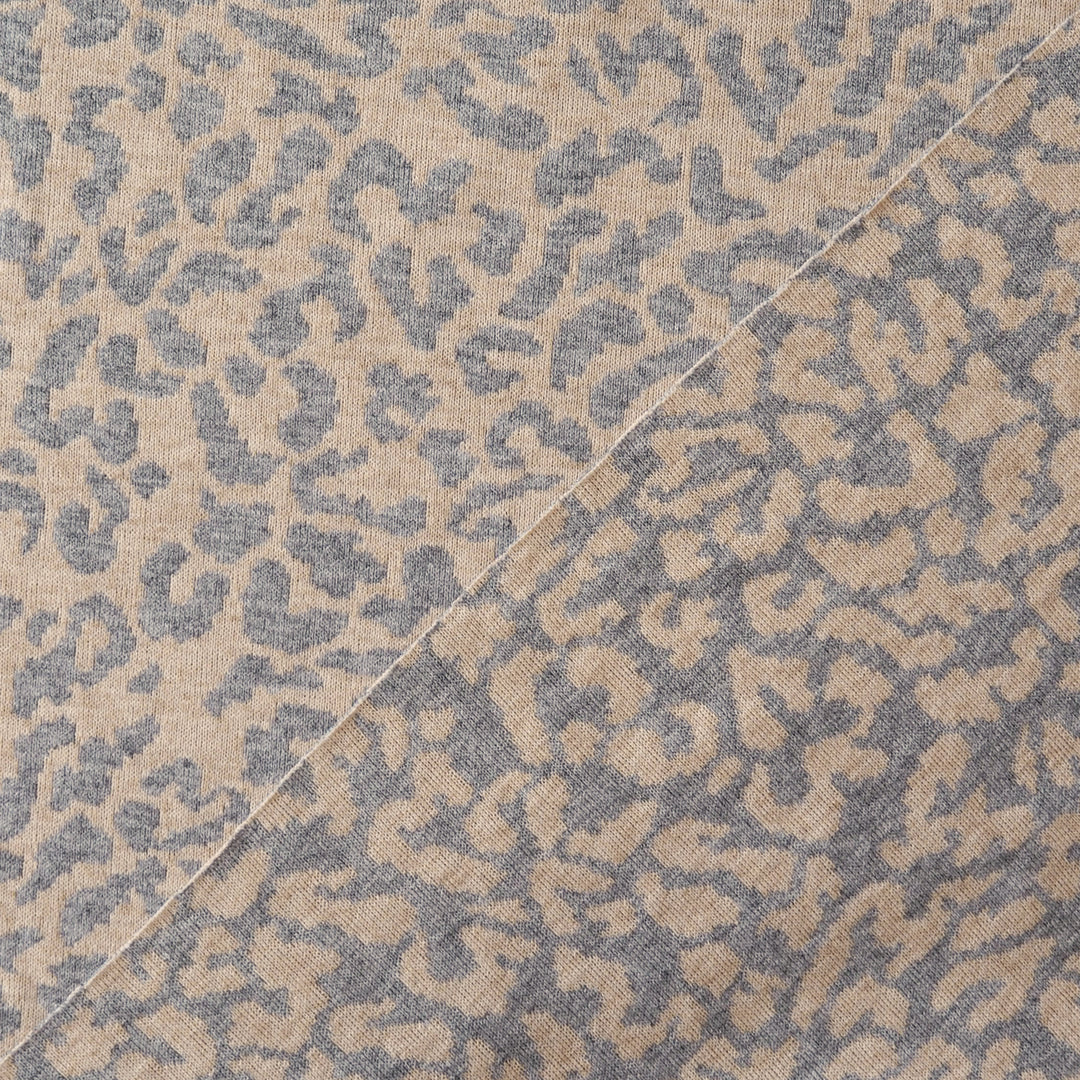 A close-up of a woven fabric with an abstract leopard-like pattern in beige and slate blue-gray, divided diagonally by a light-colored seam.