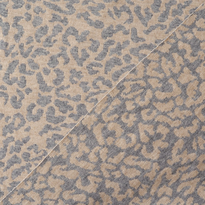 A close-up of a woven fabric with an abstract leopard-like pattern in beige and slate blue-gray, divided diagonally by a light-colored seam.