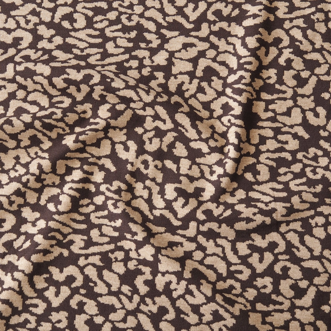 A close-up of draped fabric with an abstract leopard-like pattern in warm beige/tan and dark brown.