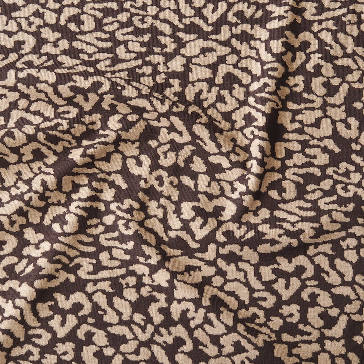 A close-up of draped fabric with an abstract leopard-like pattern in warm beige/tan and dark brown.