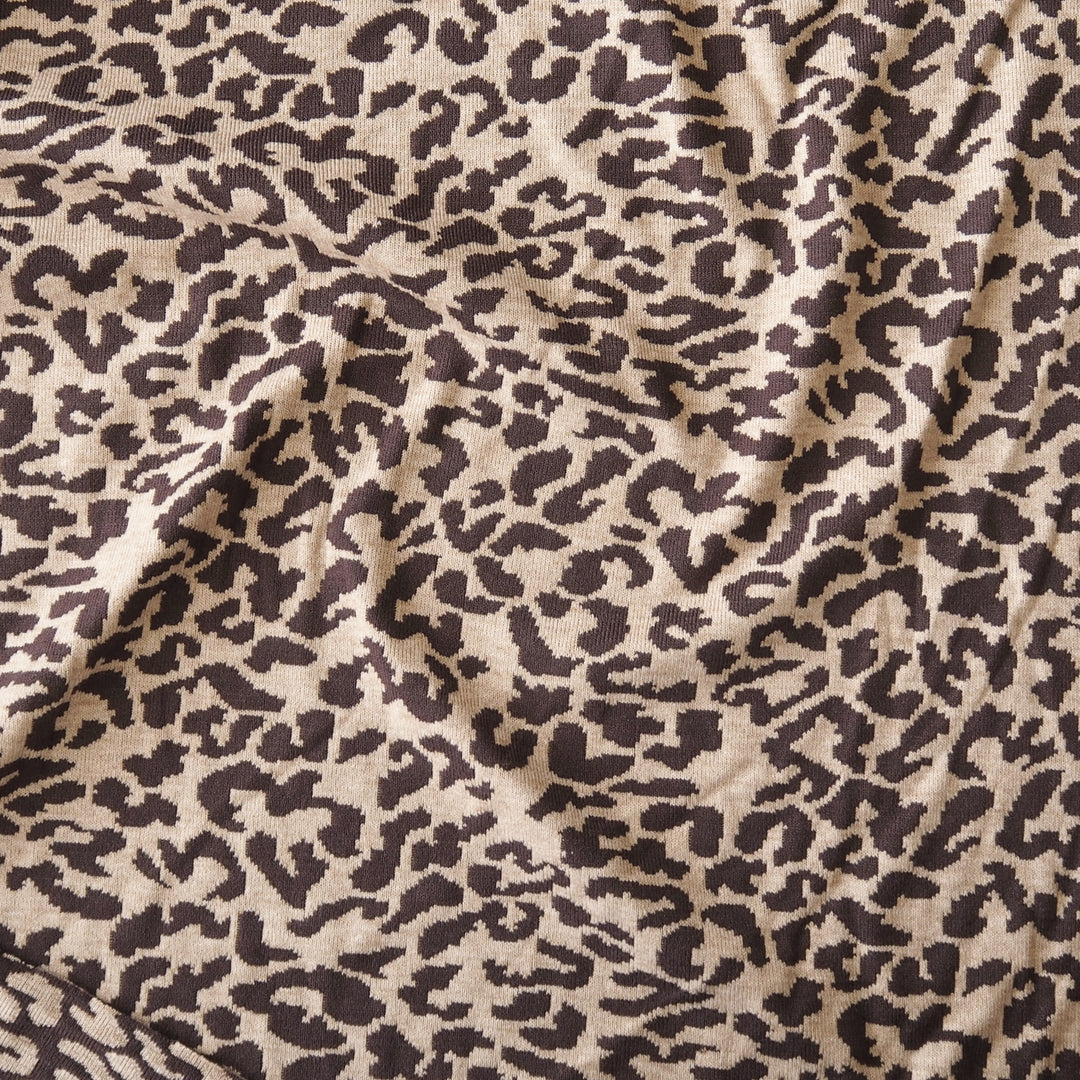 A close-up of leopard print fabric with dark brown irregular spots on a warm beige background, shown with soft folds and texture.