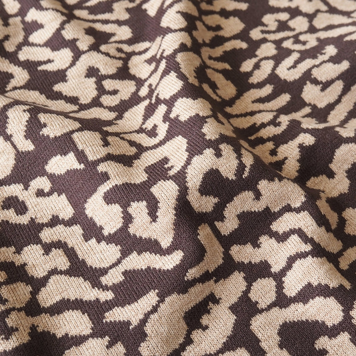 Close-up of a knitted fabric with an abstract leopard-like pattern in dark brown and warm beige.
