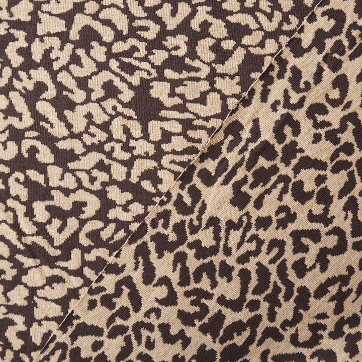 Close-up of a woven fabric with an abstract leopard-like pattern in dark brown and warm beige, with a diagonal seam visible.