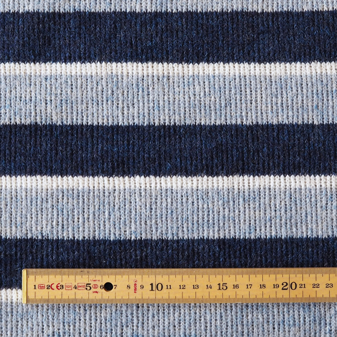 A close-up of a striped knit fabric with horizontal bands of navy blue, light blue, and white, shown with a wooden ruler at the bottom for scale.