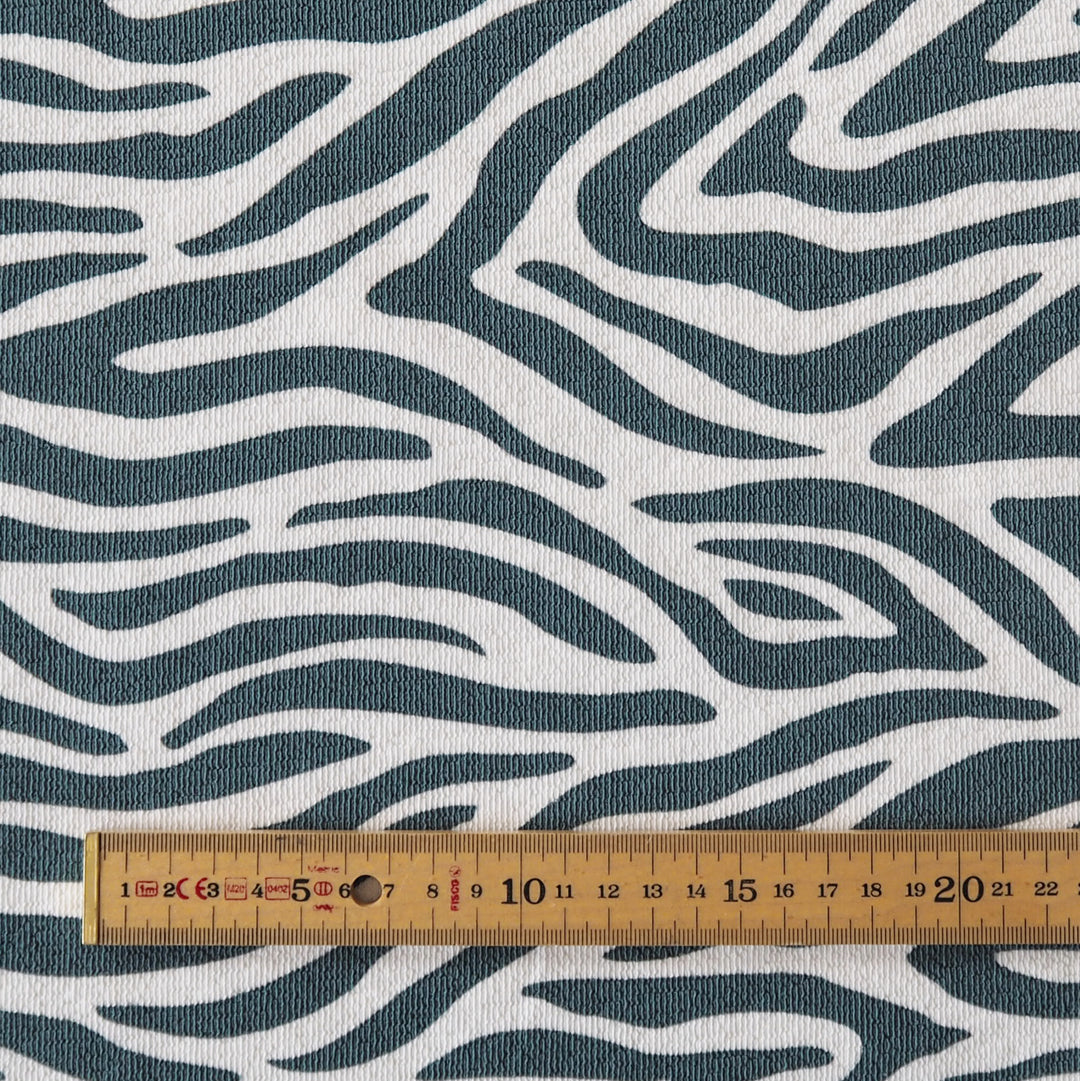 A close-up of a fabric with a wavy zebra-like pattern in dark teal and off-white, with a wooden ruler at the bottom for scale.