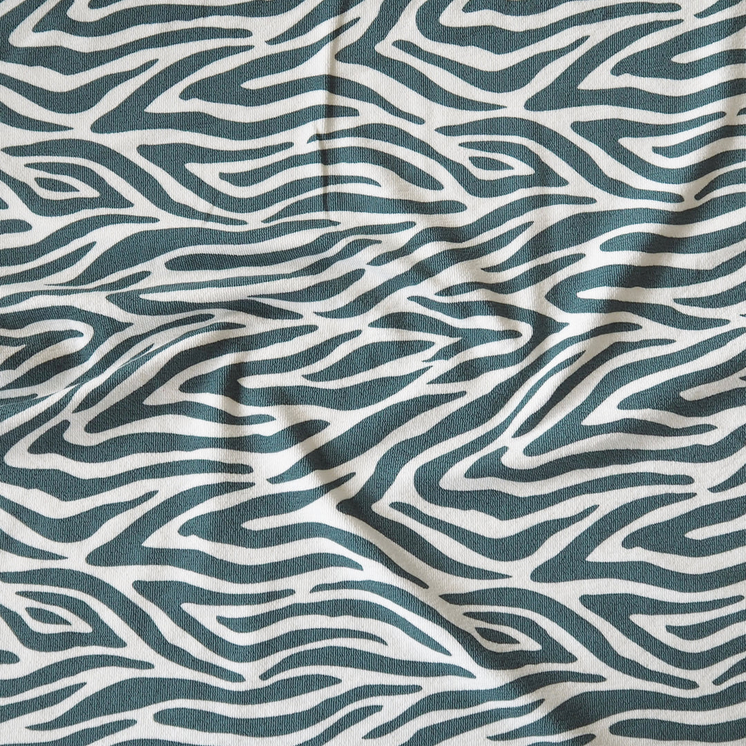 A close-up of a fabric with an abstract wavy zebra-like pattern in dark teal and off-white, showing soft folds and texture.