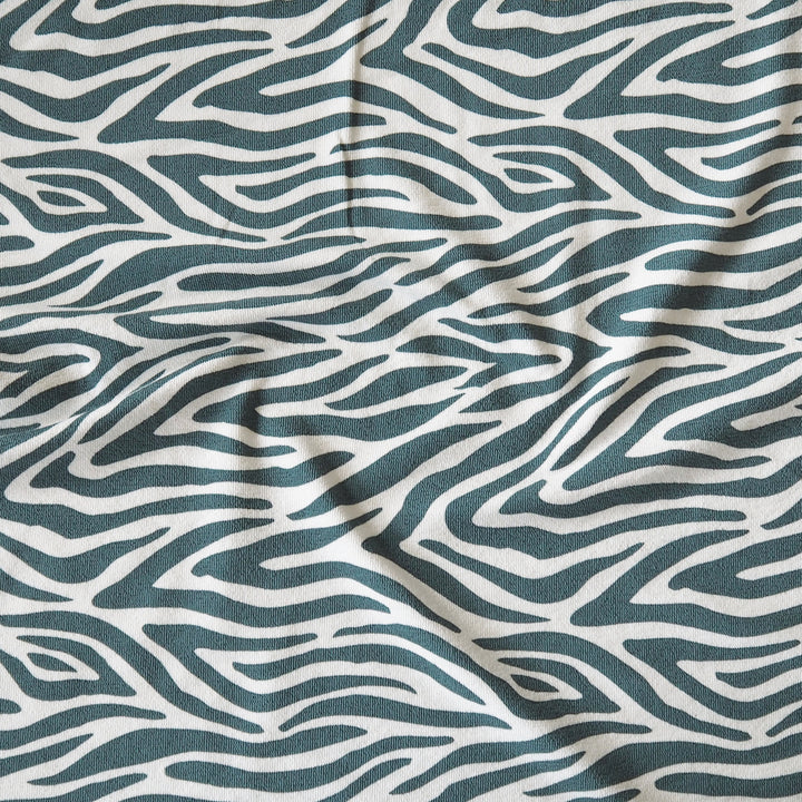 A close-up of a fabric with an abstract wavy zebra-like pattern in dark teal and off-white, showing soft folds and texture.