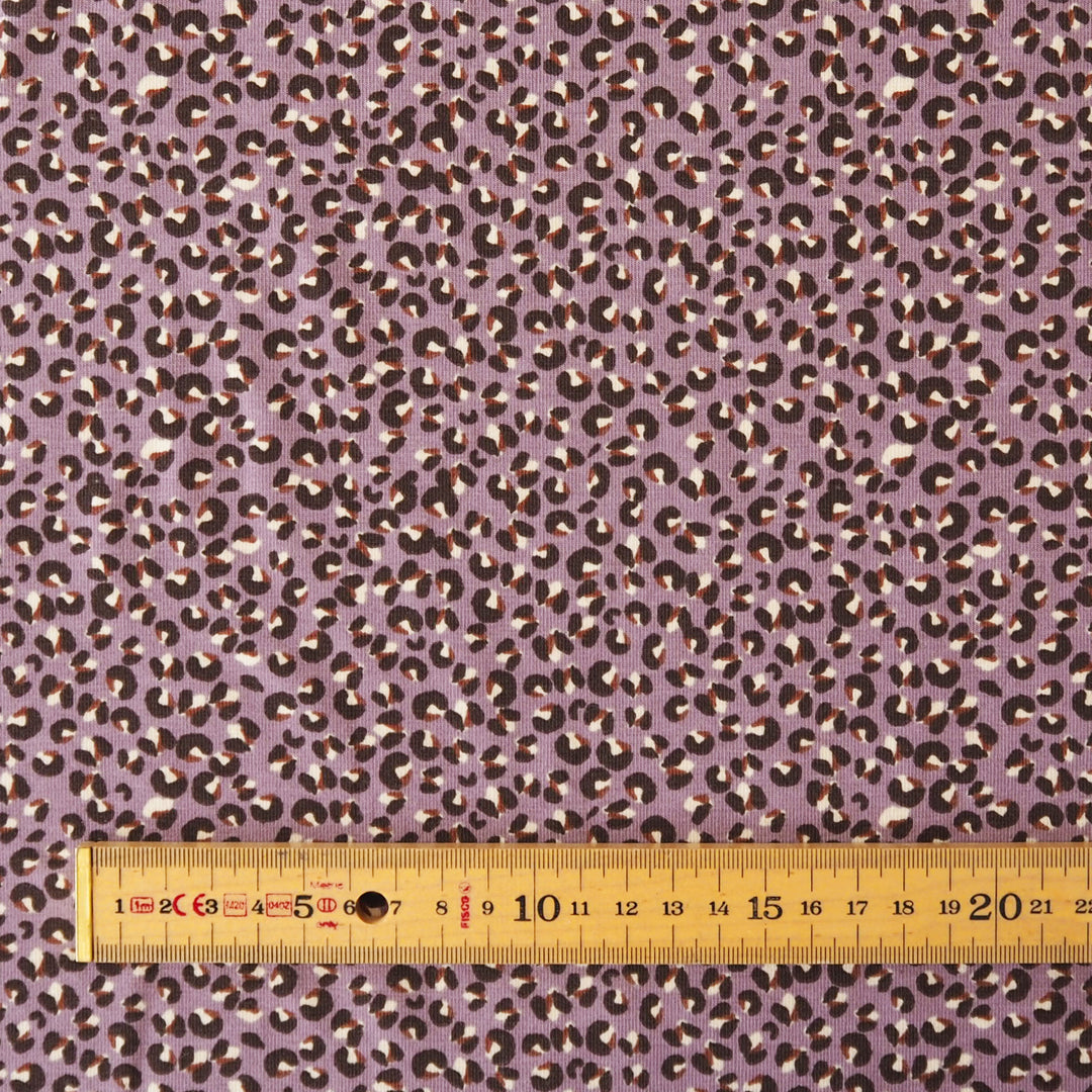 A close-up of a purple leopard print fabric with a wooden ruler at the bottom to show scale.