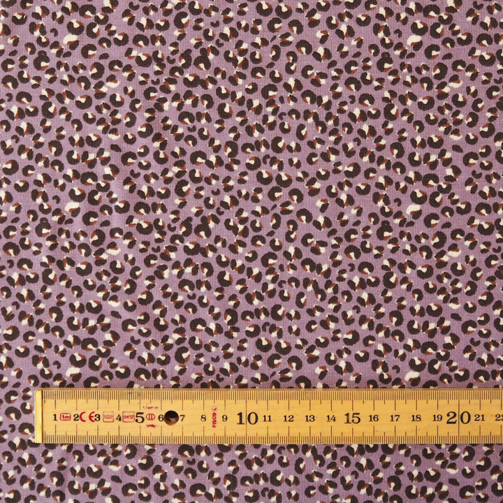 A close-up of a purple leopard print fabric with a wooden ruler at the bottom to show scale.