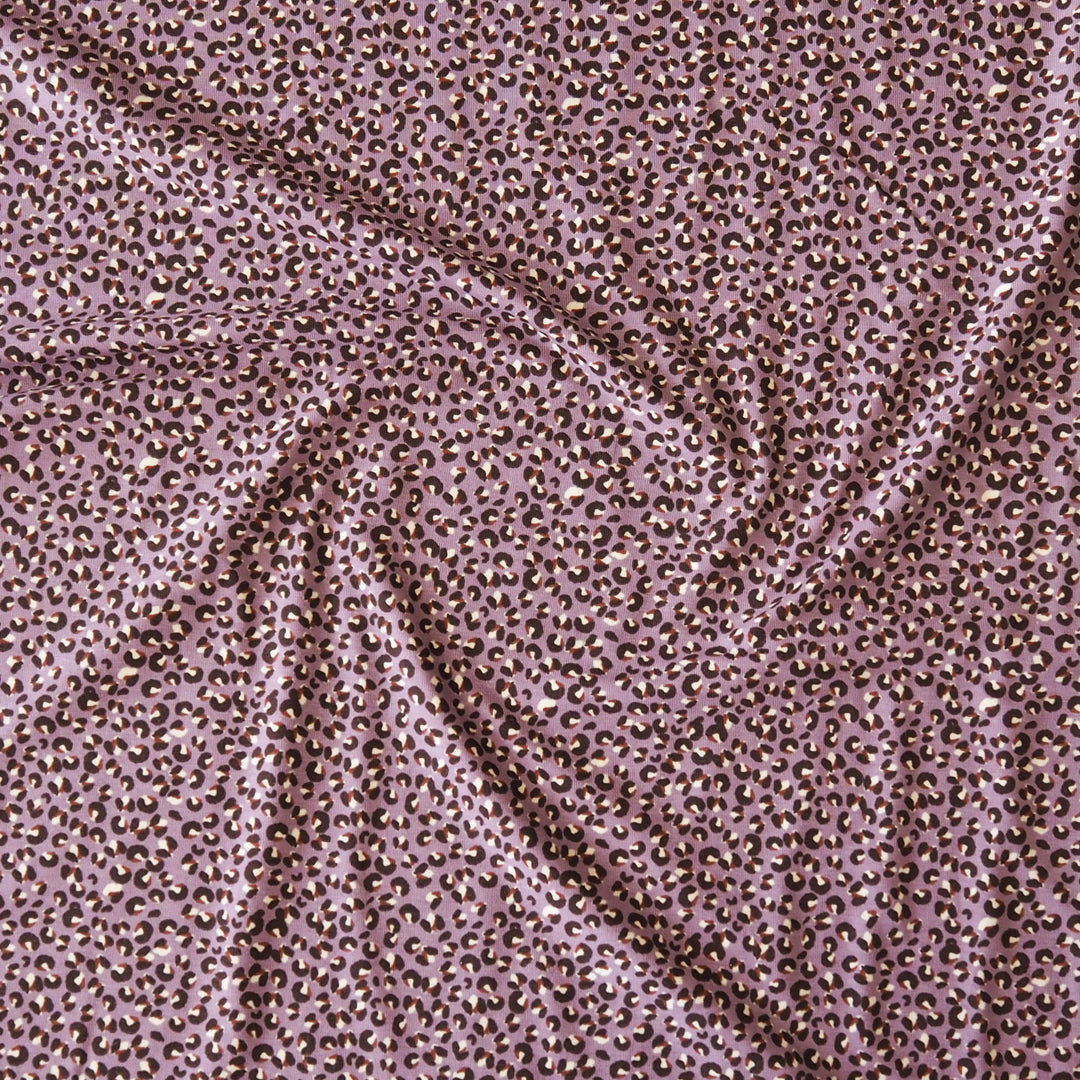 A close-up of draped fabric with an allover small leopard-like spot pattern in brown and black on a dusty mauve-pink background.