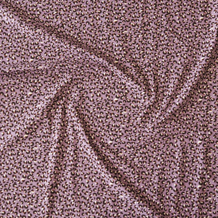 A close-up of draped fabric with an allover small leopard-like spot pattern in brown and black on a dusty mauve-pink background.