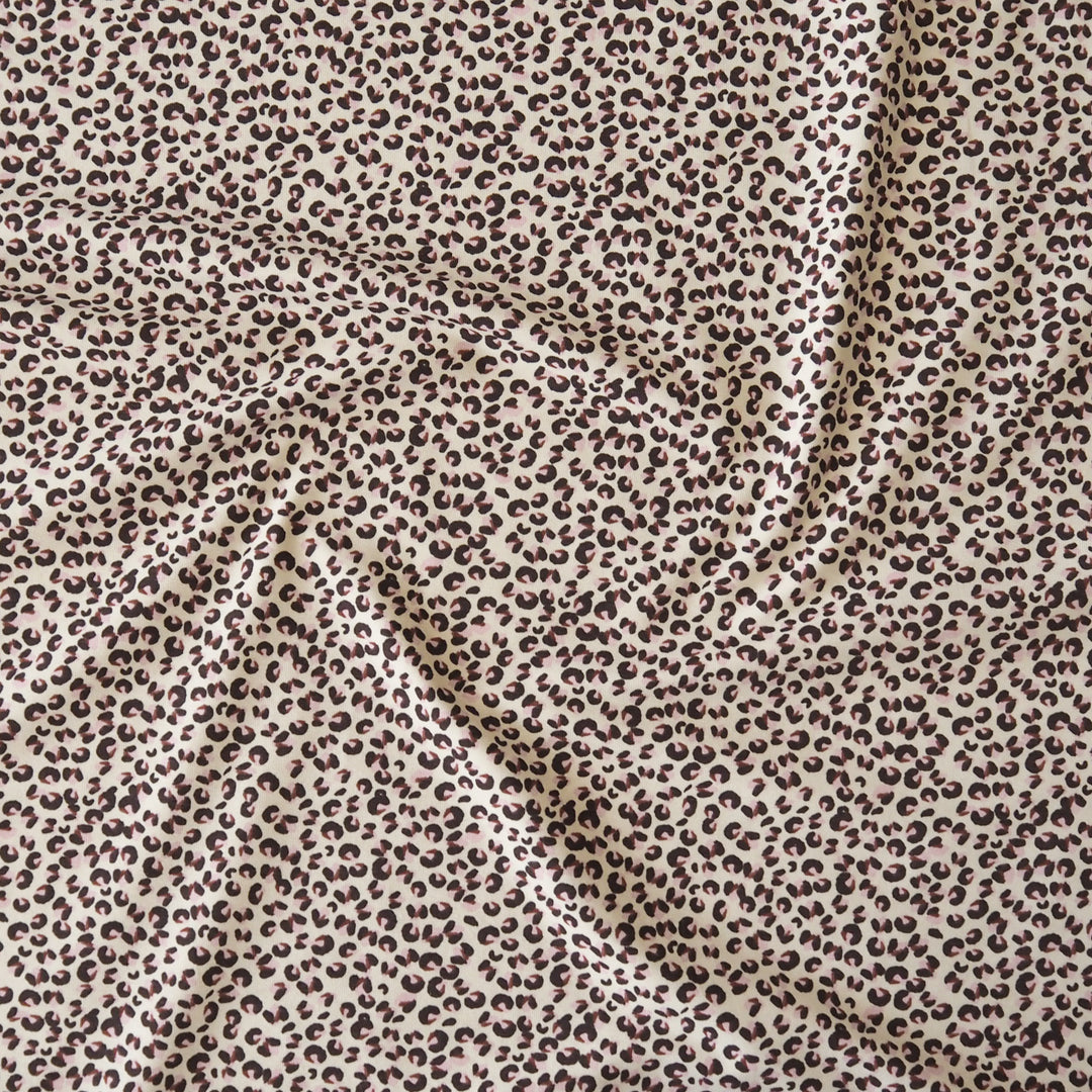 A close-up of draped fabric with an allover leopard print pattern in dark brown on a warm beige background.