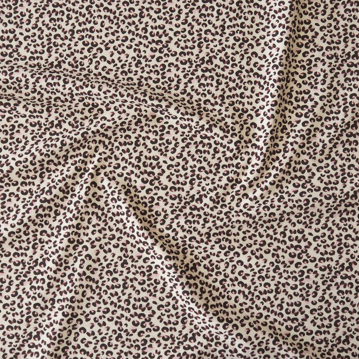 A close-up of draped fabric with an allover leopard print pattern in dark brown on a warm beige background.