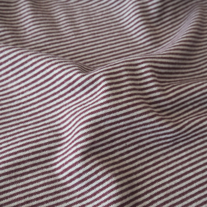 A close-up of a striped knit fabric with thin horizontal burgundy and blue stripes, showing a soft draped texture.