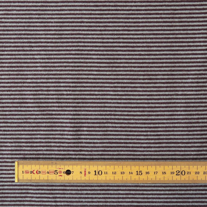 Close-up of a striped fabric with thin horizontal burgundy and blue lines, shown with a yellow measuring tape ruler along the bottom edge for scale.