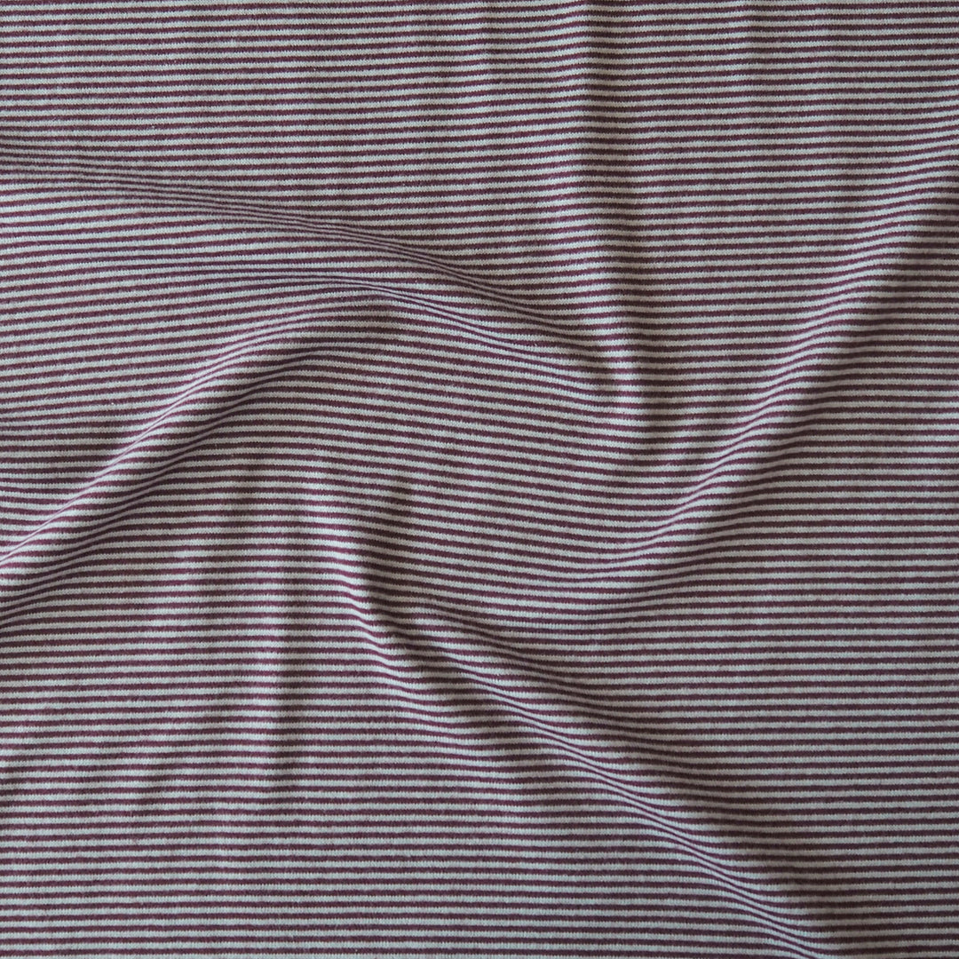 Close-up of a striped knit fabric with thin horizontal burgundy and blue stripes, shown with soft folds.