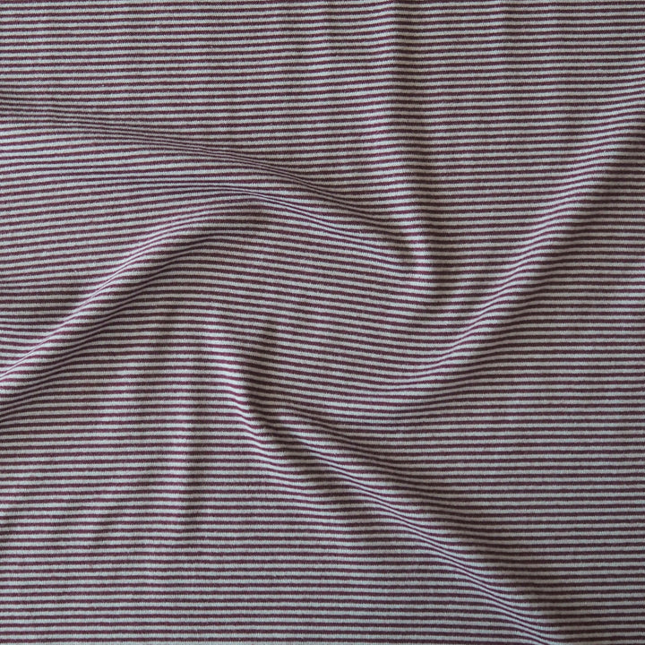 Close-up of a striped knit fabric with thin horizontal burgundy and blue stripes, shown with soft folds.