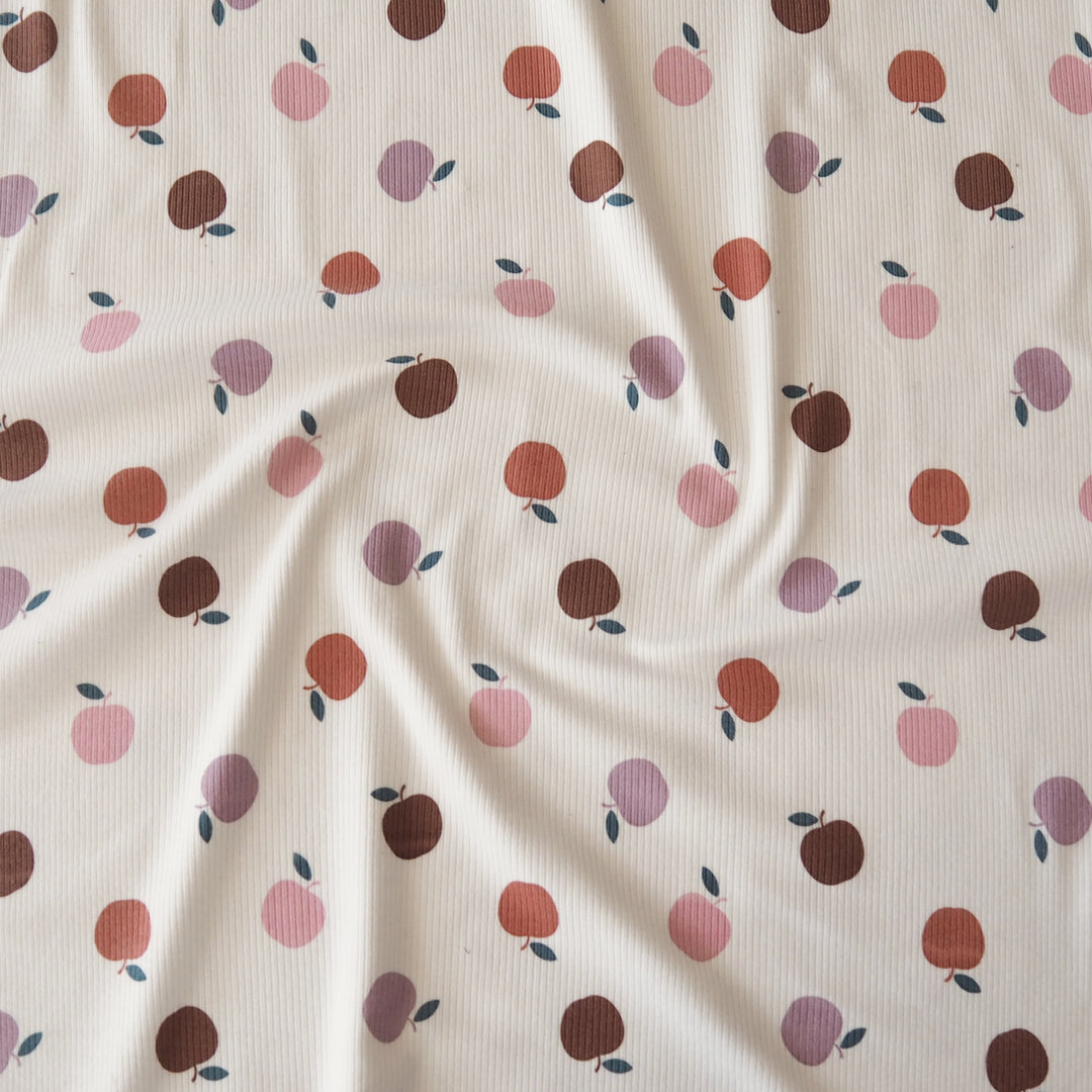 A close-up of a ribbed fabric with a repeating pattern of stylized peaches in shades of pink, rust orange, and dark brown on an off-white background.