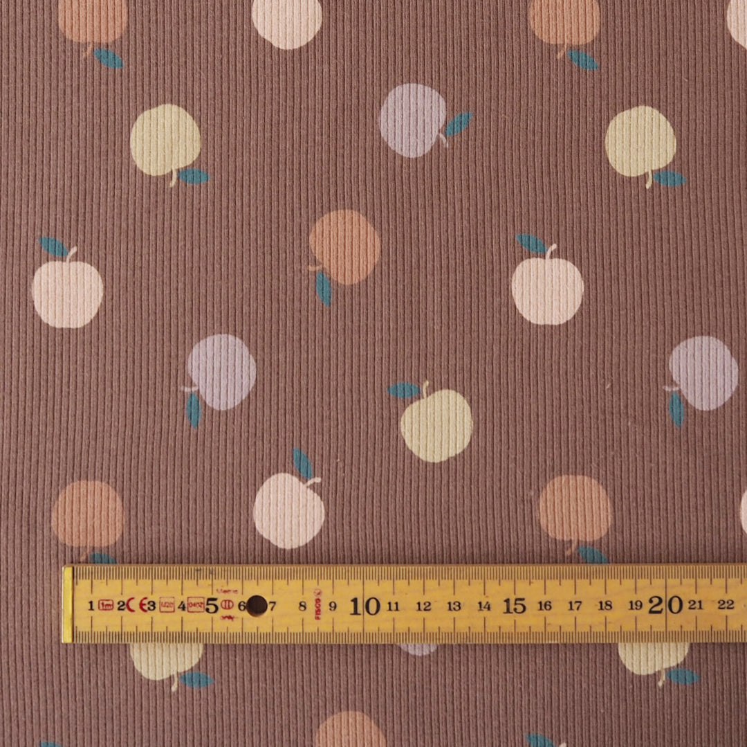 Brown ribbed fabric with a repeating pattern of stylized fruit in cream, peach, and lavender, with a yellow ruler along the bottom edge for scale.