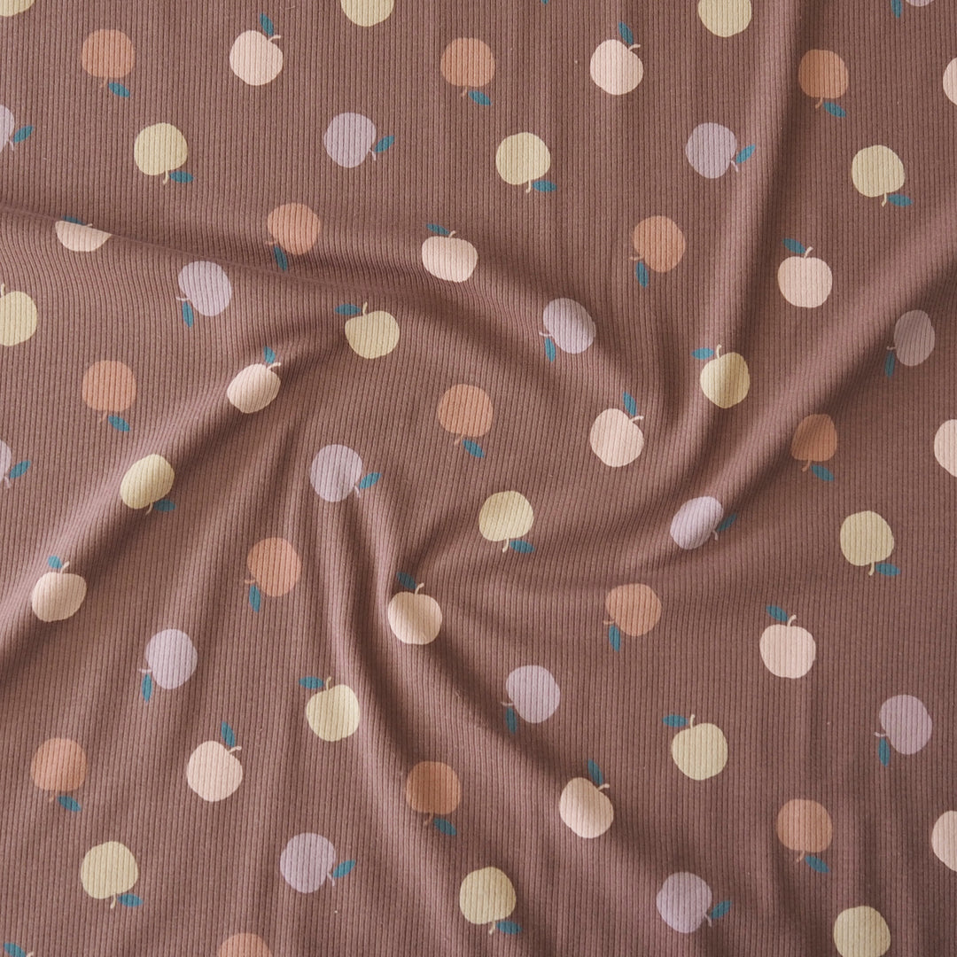 A close-up of a ribbed fabric in a dusty mauve-brown color, printed with a pattern of small fruit in pastel peach, cream, lavender, and brown with tiny blue leaves.