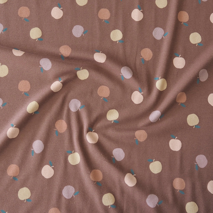 A close-up of a ribbed fabric in a dusty mauve-brown color, printed with a pattern of small fruit in pastel peach, cream, lavender, and brown with tiny blue leaves.