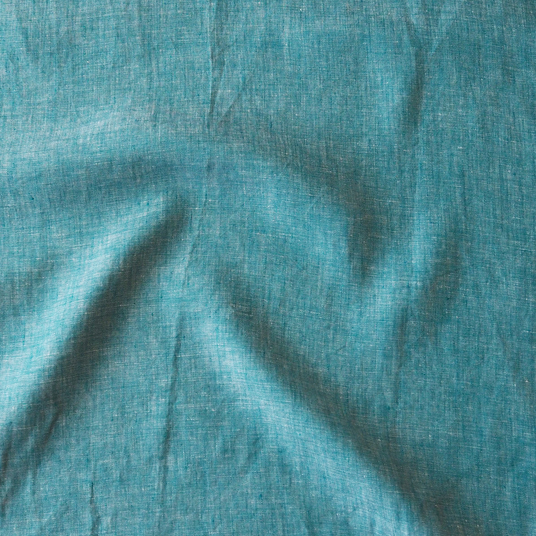 A close-up of textured fabric in a muted teal blue-green color, showing soft folds and a woven linen-like surface.