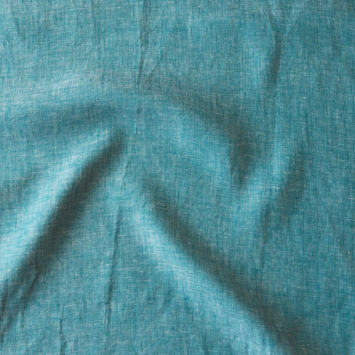 A close-up of textured fabric in a muted teal blue-green color, showing soft folds and a woven linen-like surface.