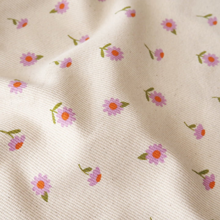Close-up of a cream-colored woven fabric with a delicate pattern of small pink and purple flowers with orange centers and green stems.