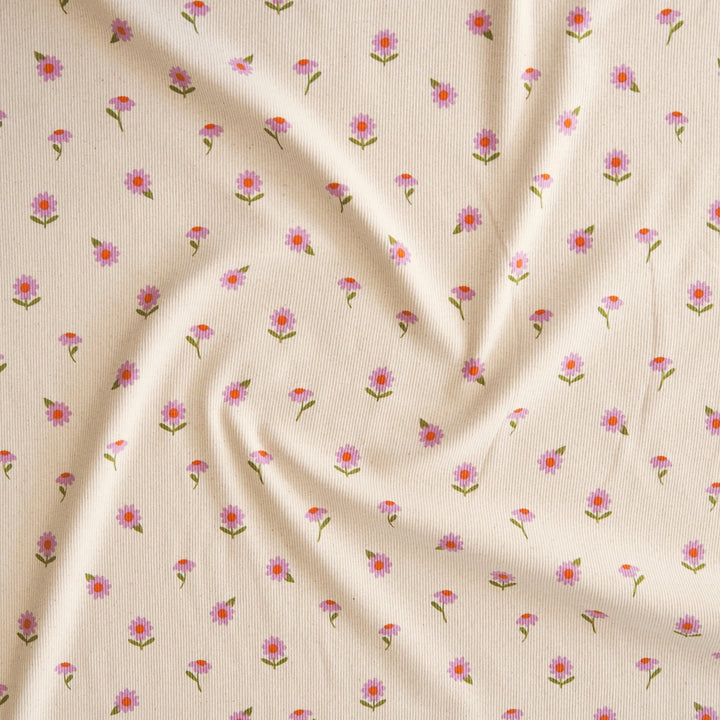 A close-up of a cream-colored fabric with a delicate, repeating pattern of small pink and purple flowers with green stems, arranged in soft folds.
