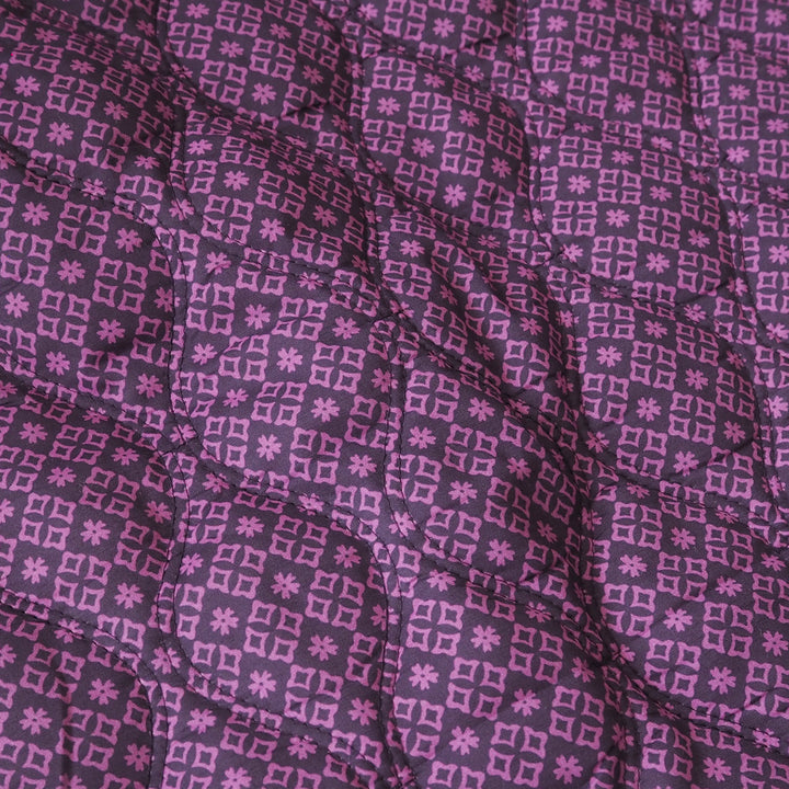 A close-up of a quilted fabric with a repeating geometric pattern in shades of purple and pink.