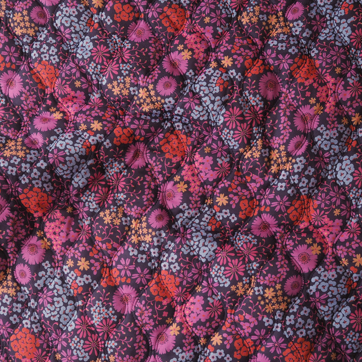 A close-up of a quilted fabric with a dense floral pattern in shades of pink, red, orange, and light blue on a dark purple background.
