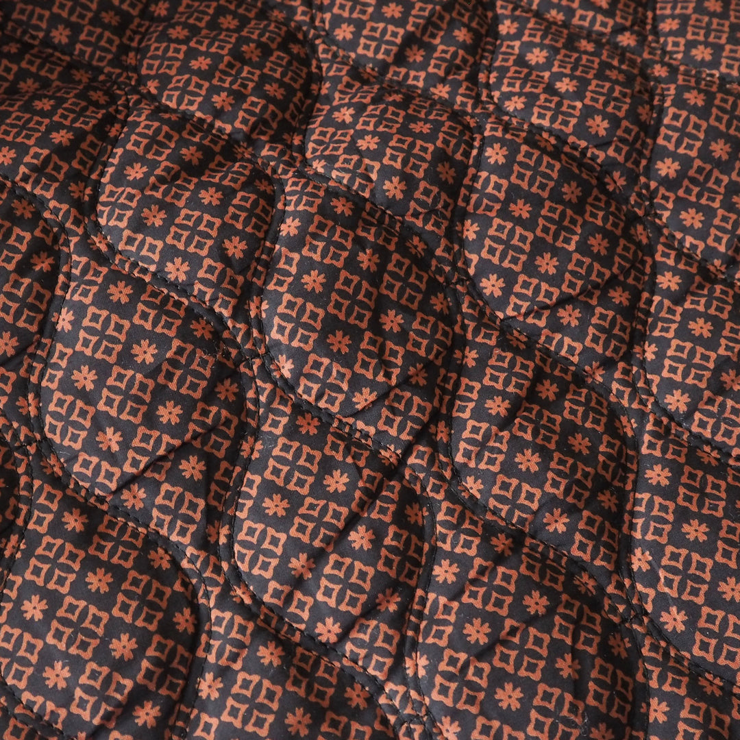 Close-up of a quilted fabric with a repeating geometric pattern in terracotta orange and dark charcoal gray.