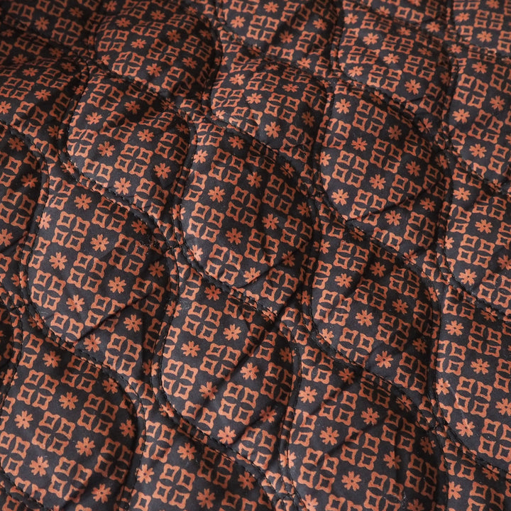 Close-up of a quilted fabric with a repeating geometric pattern in terracotta orange and dark charcoal gray.