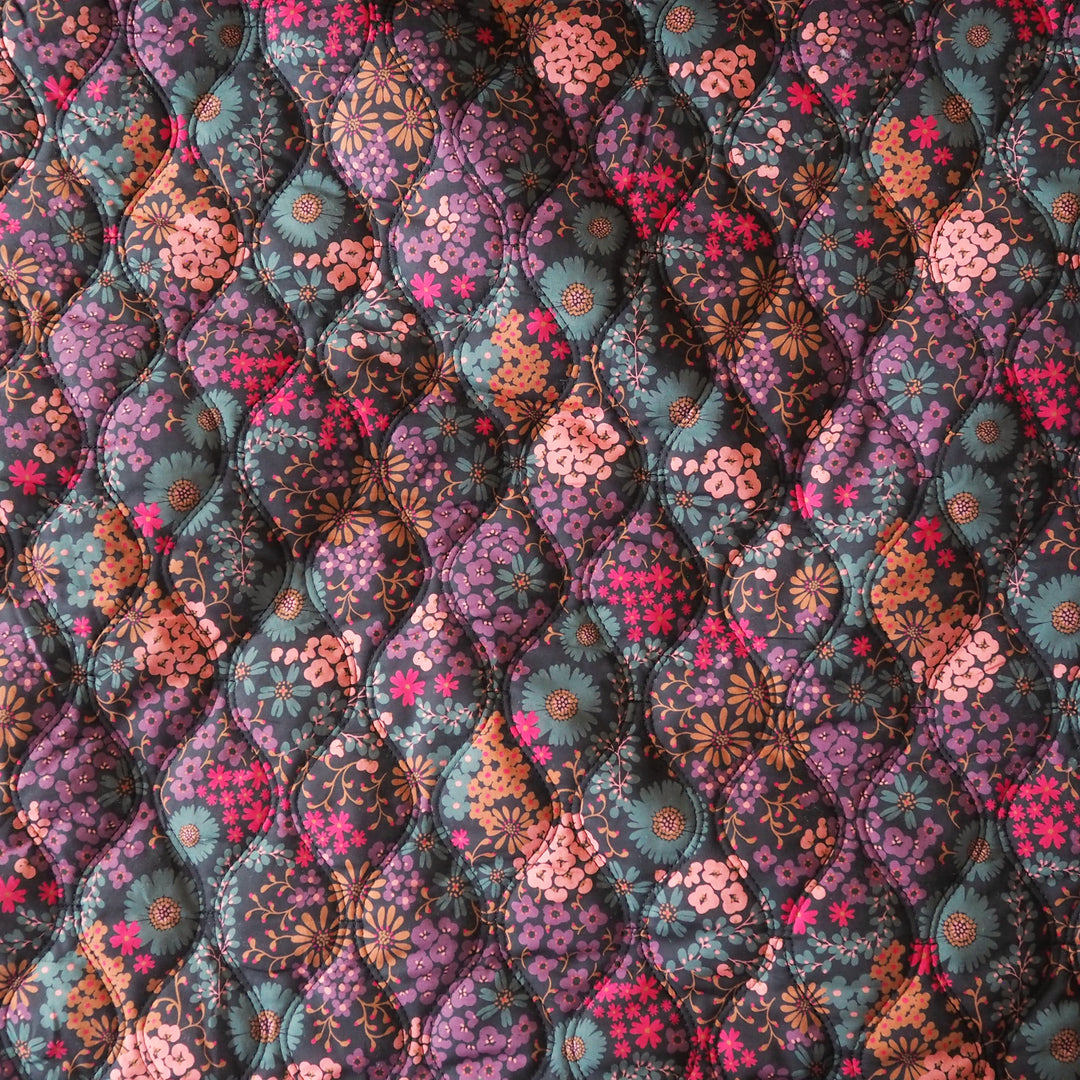 A close-up of a quilted fabric with a repeating diamond pattern featuring floral and starburst motifs in purple, teal, pink, orange, and brown tones.