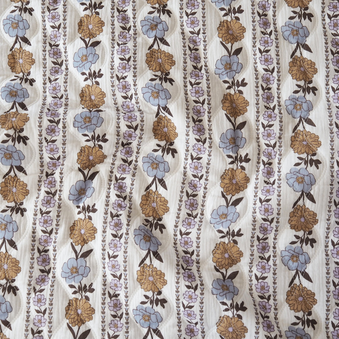 A close-up of a patterned fabric featuring vertical wavy stripes with blue, tan, and brown floral motifs on a cream background.