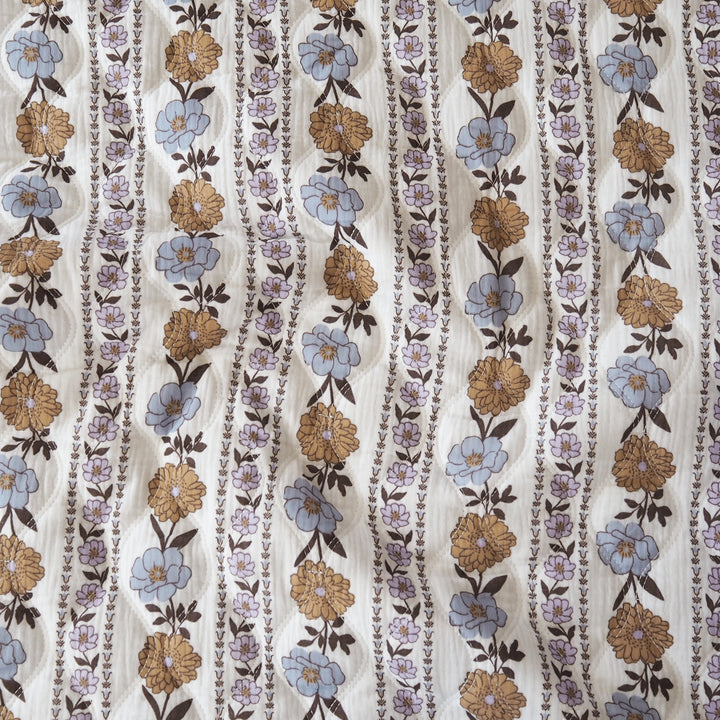 A close-up of a patterned fabric featuring vertical wavy stripes with blue, tan, and brown floral motifs on a cream background.