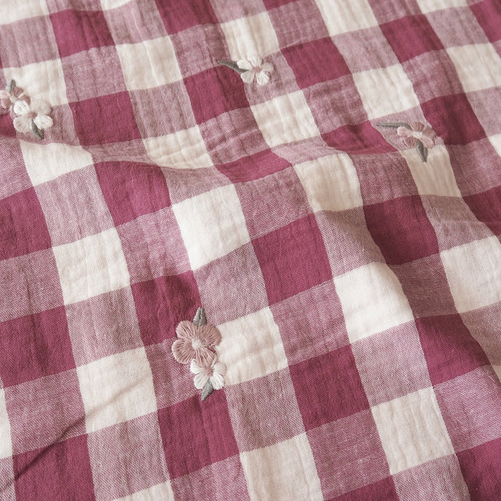 A close-up of a pink and cream gingham fabric with small embroidered floral details.