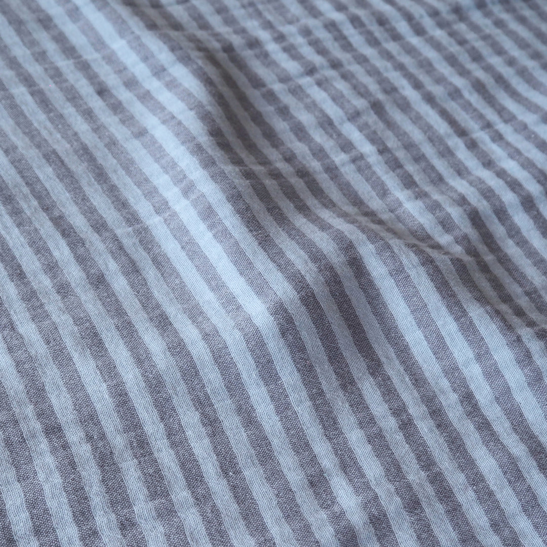 Close-up of a striped fabric with alternating light gray and medium gray vertical stripes, showing a soft woven texture and gentle folds.