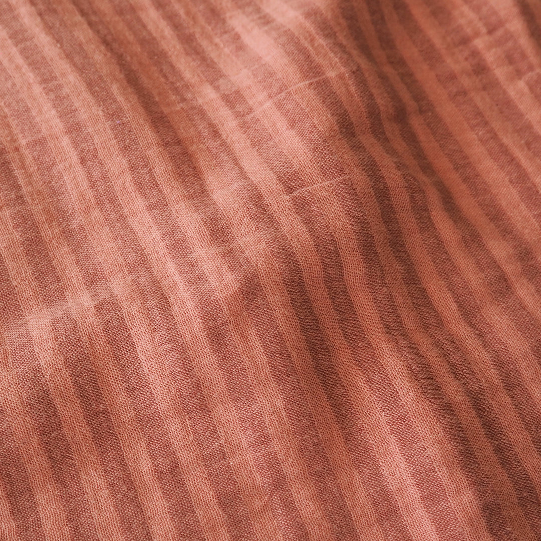 A close-up of a textured fabric with vertical stripes in dusty rose, terracotta, and brown tones.