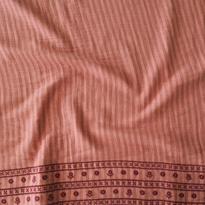 A close-up of a terracotta pink striped fabric with a decorative border pattern along the bottom edge.