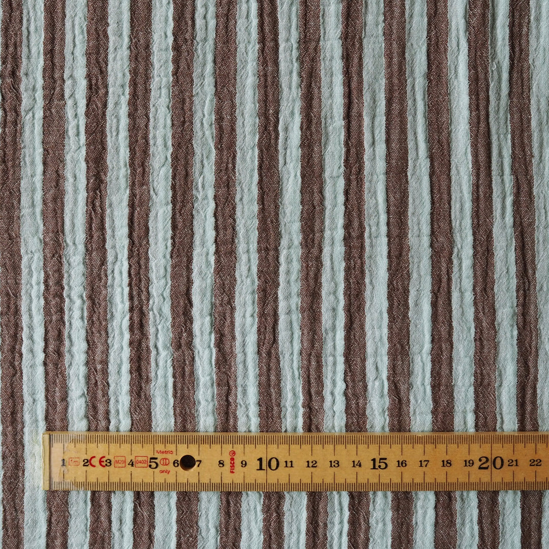 A close-up of a striped fabric with alternating vertical bands of taupe-brown and light gray, shown with a wooden ruler at the bottom for scale.