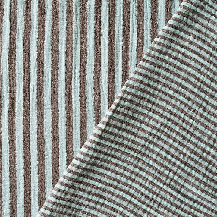 A close-up of a textured cotton muslin fabric with vertical brown and pale mint green stripes, folded diagonally to show its soft texture.